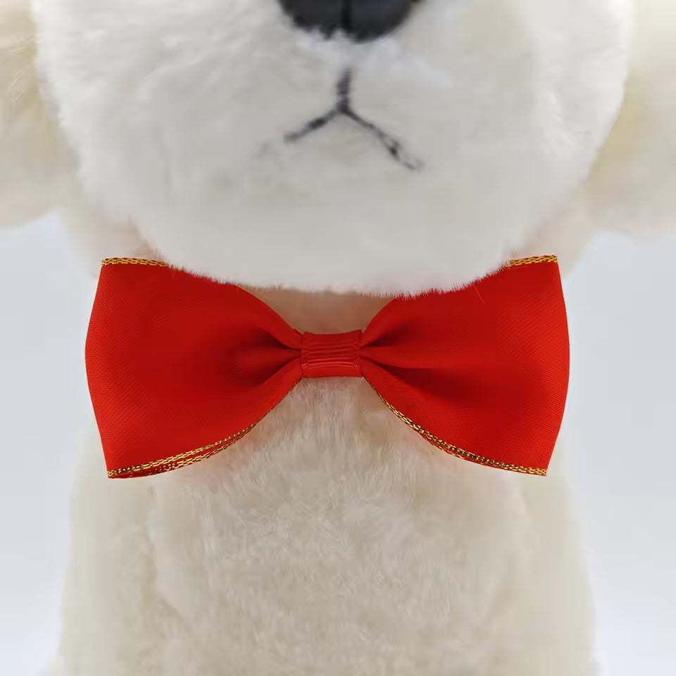 Close-up of a white plush dog model wearing a classic red Christmas pet bow tie with gold edging.